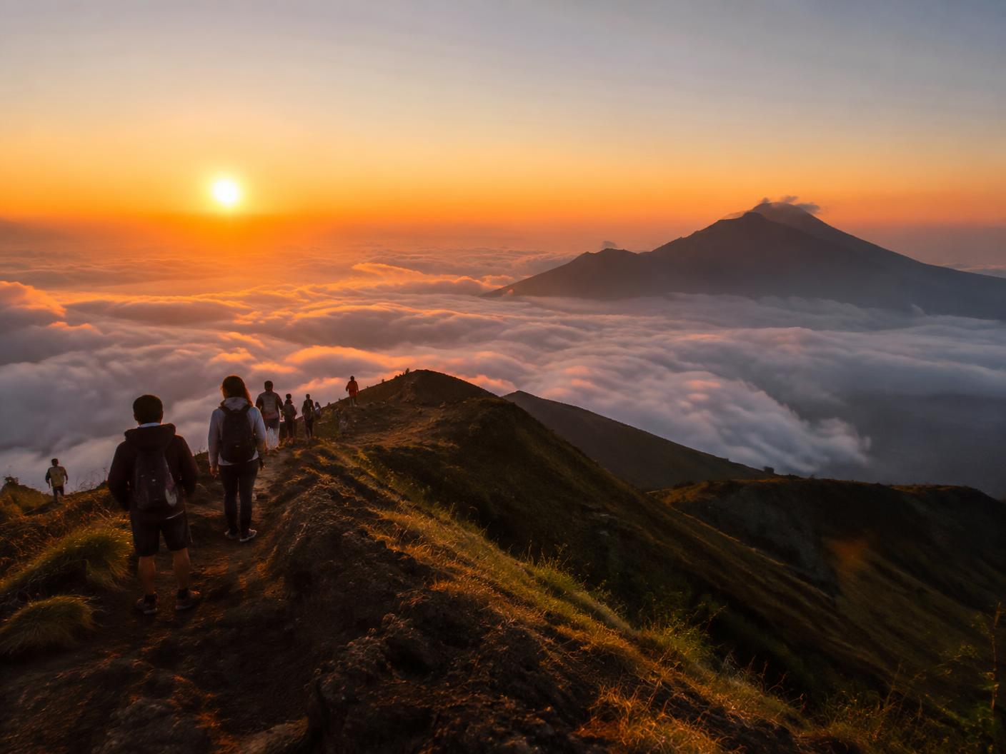 Hikers on a volcanic ridge at sunrise above the clouds